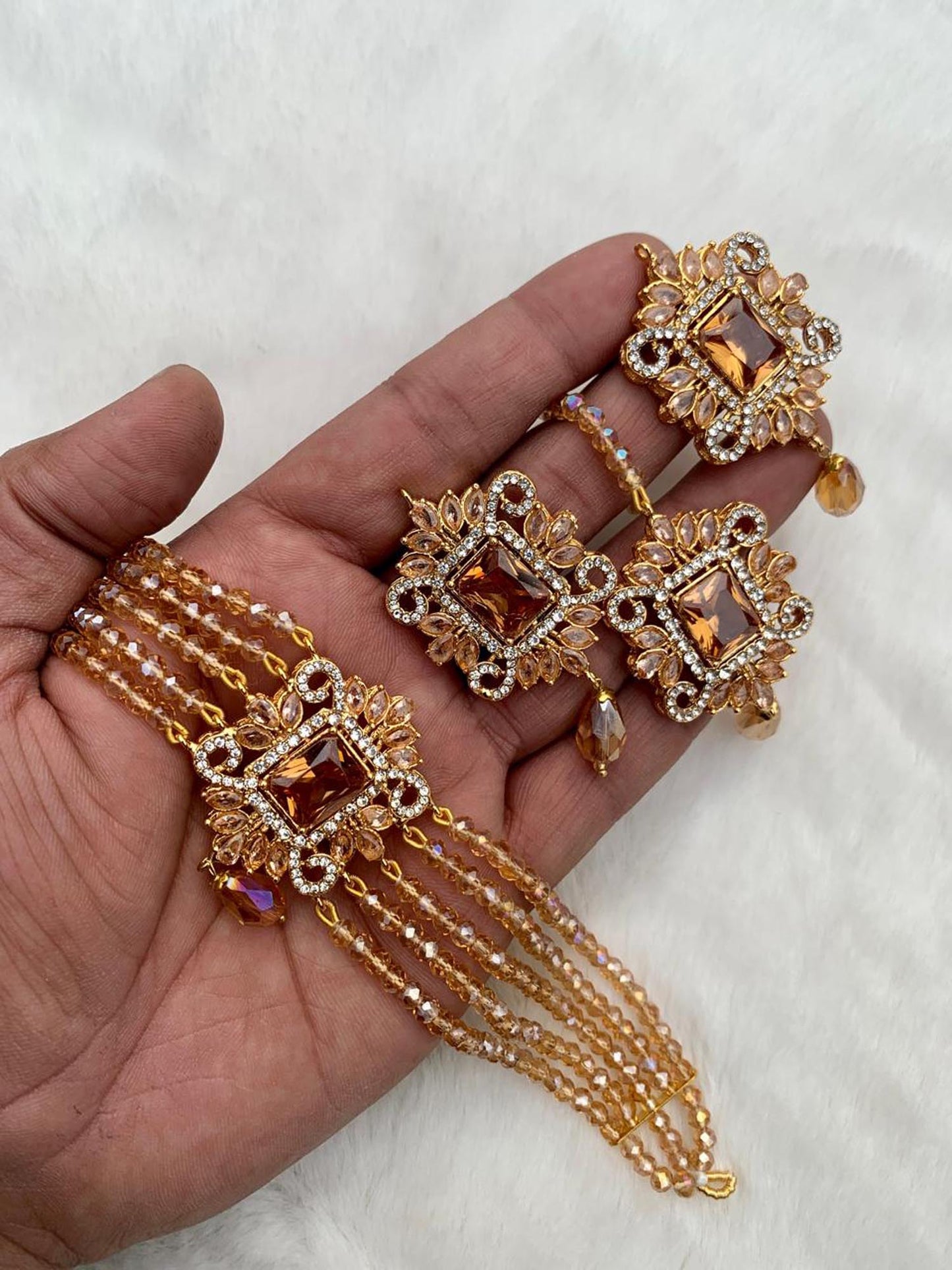 hand holding a golden pakistani choker set with earrings and matching maang tikka high quality pakistani jewellery