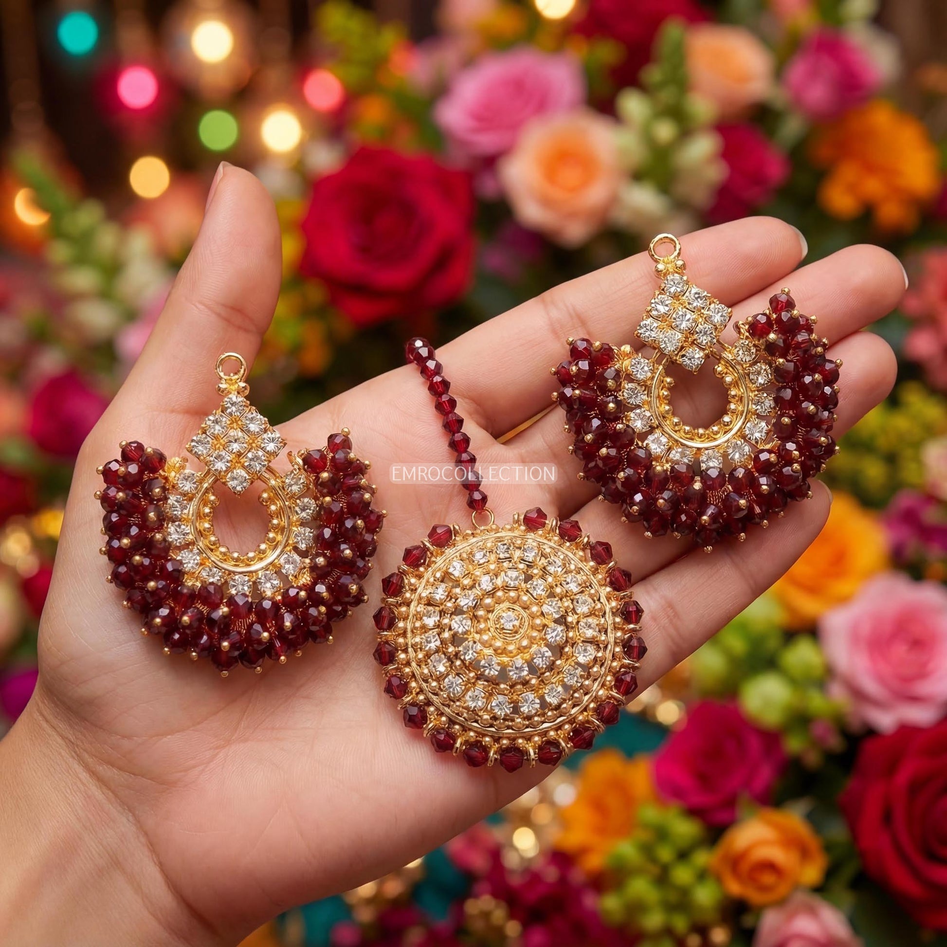 Hand holding maroon chand bali earrings and tikka with a colorful floral background