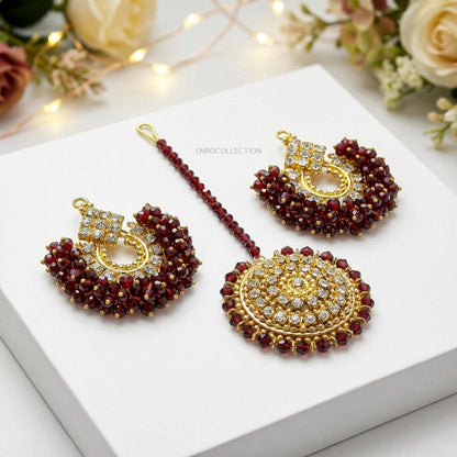 maroon and golden hue chand bai earrings tikka on a white surface with floral decorations.