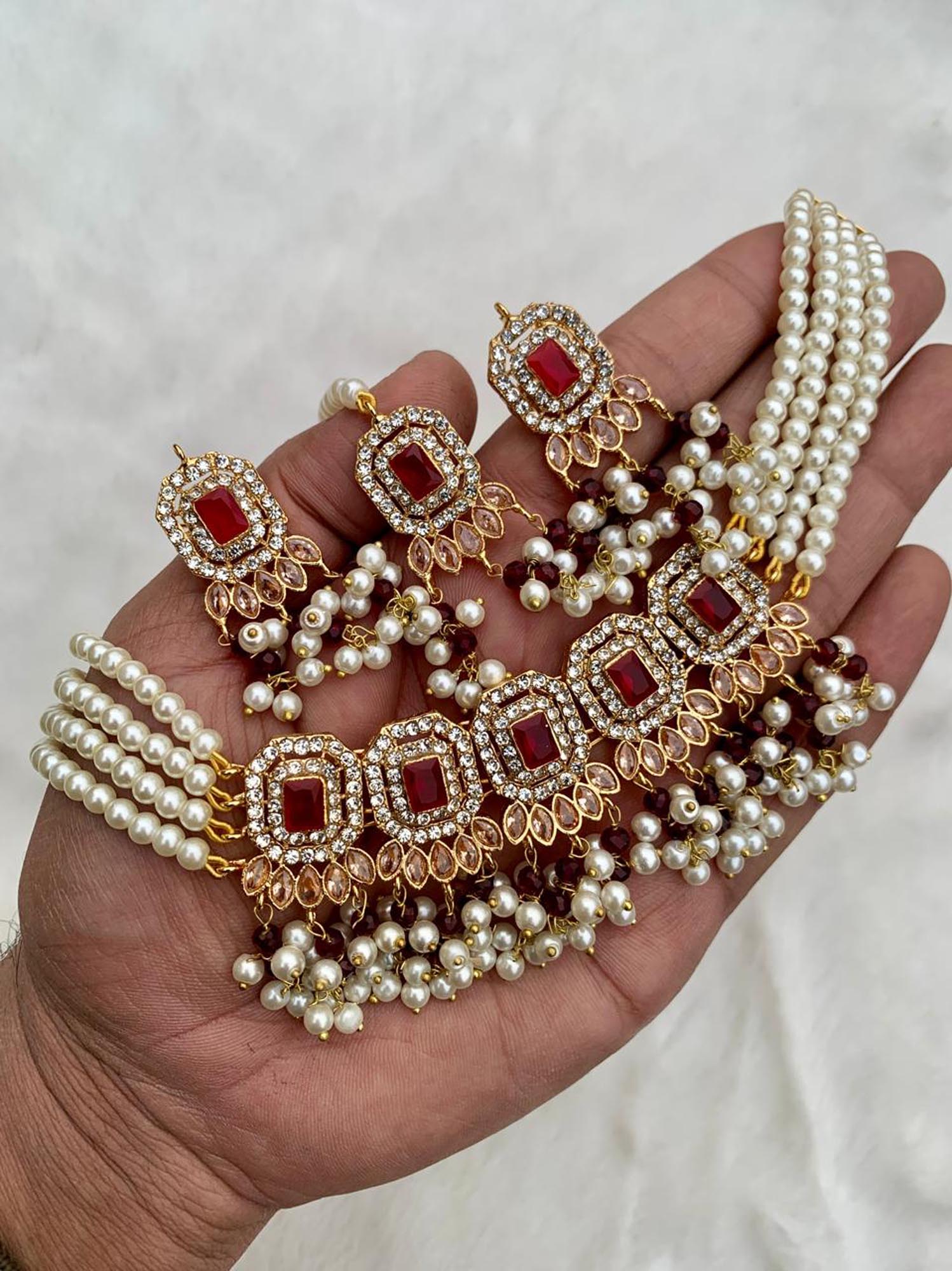 Hand holding a set of pearl and maroon choker necklace on a light background pakistani jewellery
