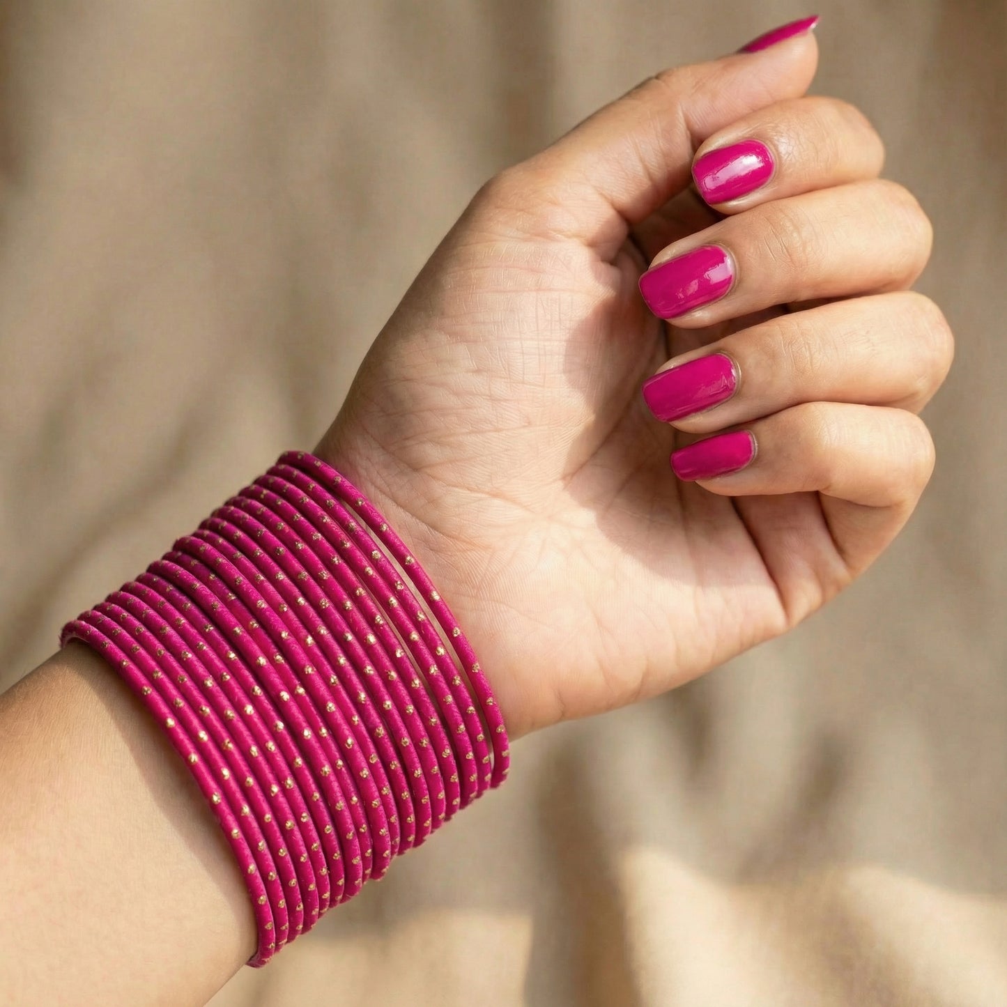 close-up of model wrist wearing shocking pink bangles with golden dots showing vibrant colour and festive indian jewellery look indian jewellery