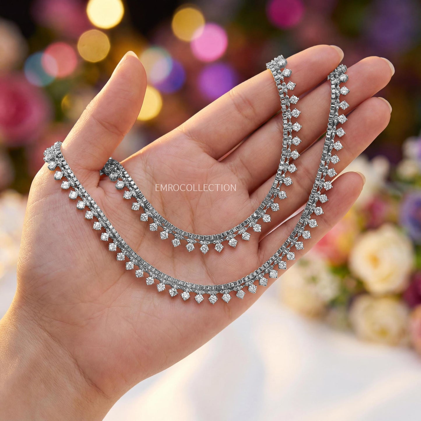 silver anklets held in a hand with a blurred colorful background