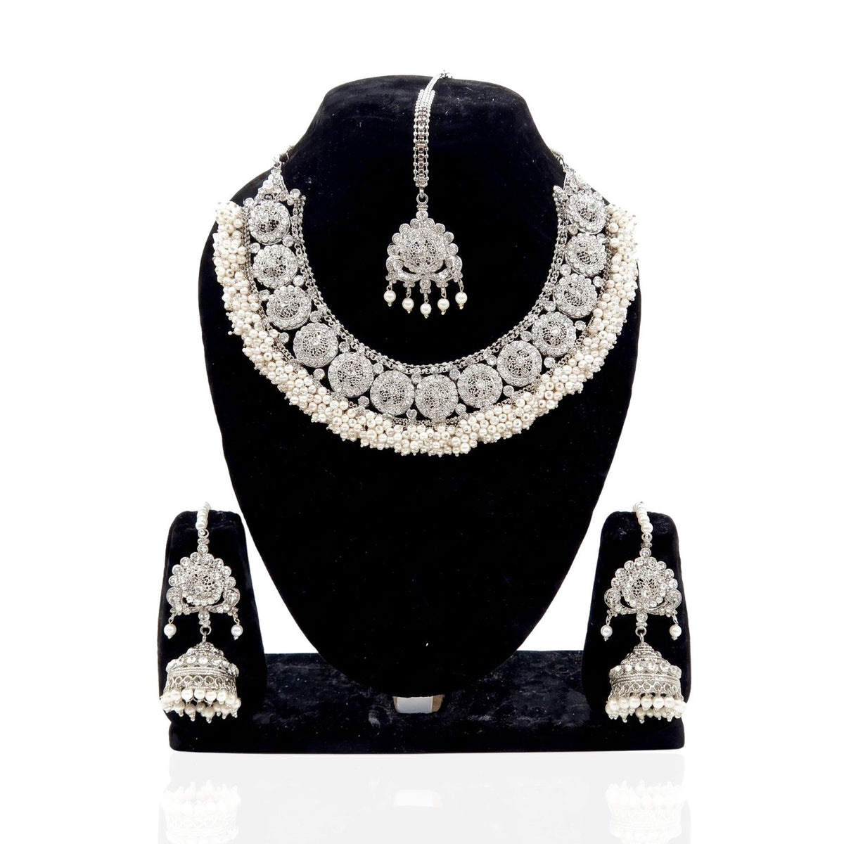 A silver-toned traditional Indian jewelry set displayed on a black velvet mannequin bust, including a choker necklace, matching maang tikka, and jhumka earrings.