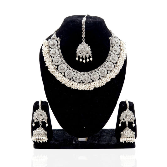 A silver-toned traditional Indian jewelry set displayed on a black velvet mannequin bust, including a choker necklace, matching maang tikka, and jhumka earrings.