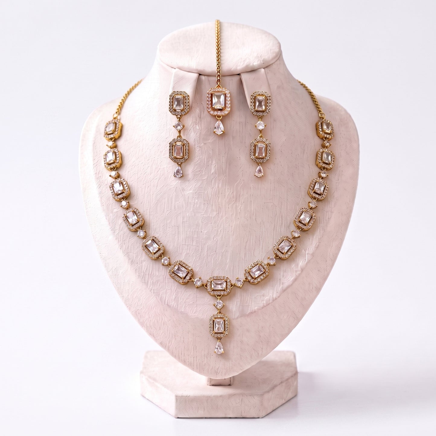 the simple gold and white necklace, earrings and tikka set arranged together on a plain backdrop