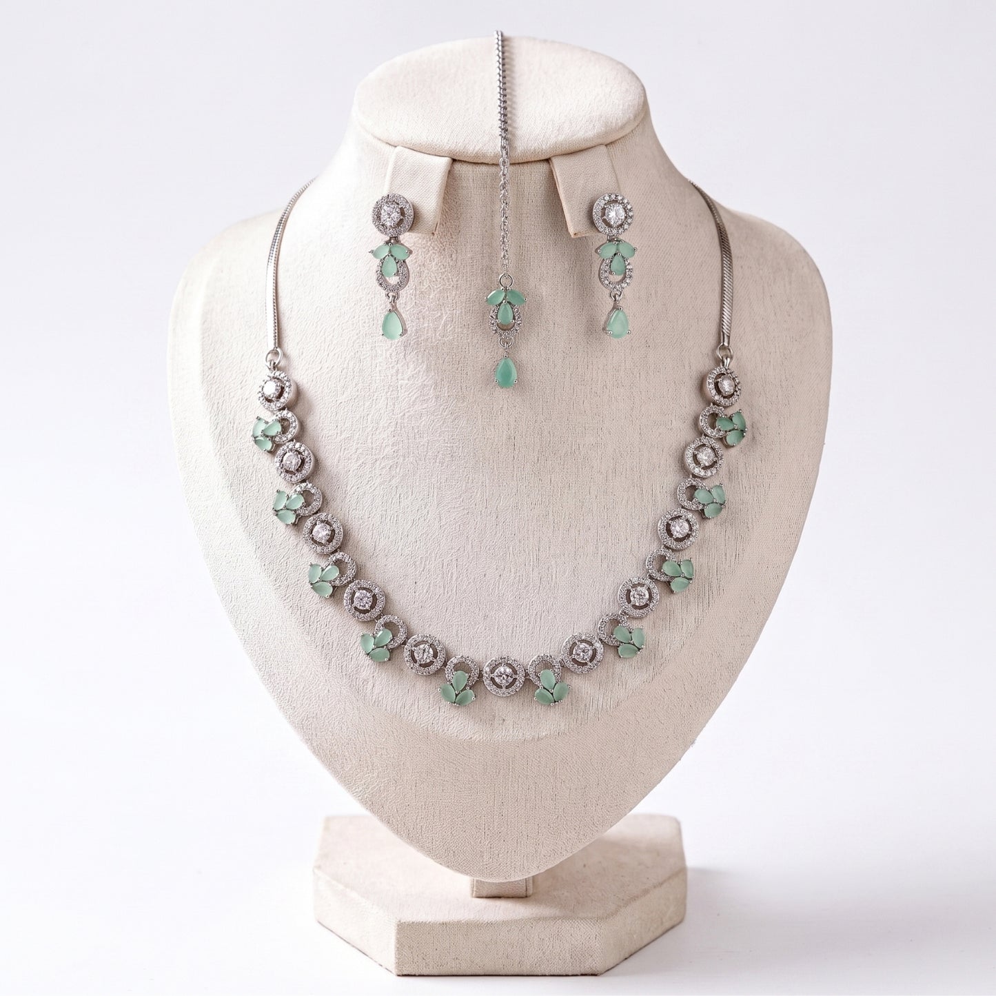 the simple silver and mint necklace, earrings and tikka set laid out together on a plain surface
