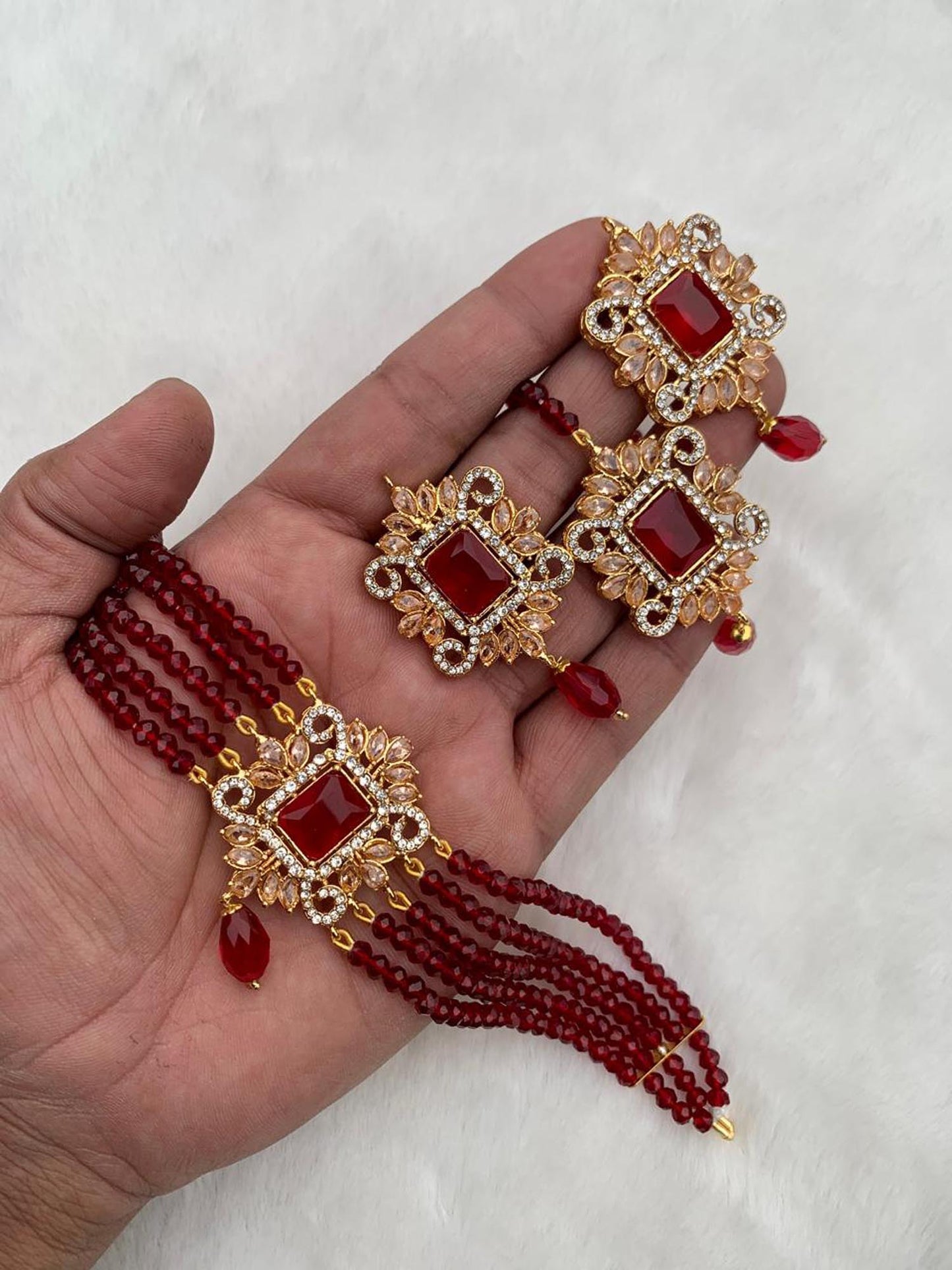 gold and maroon jewelry set on a hand with a white background pakistani jewellery