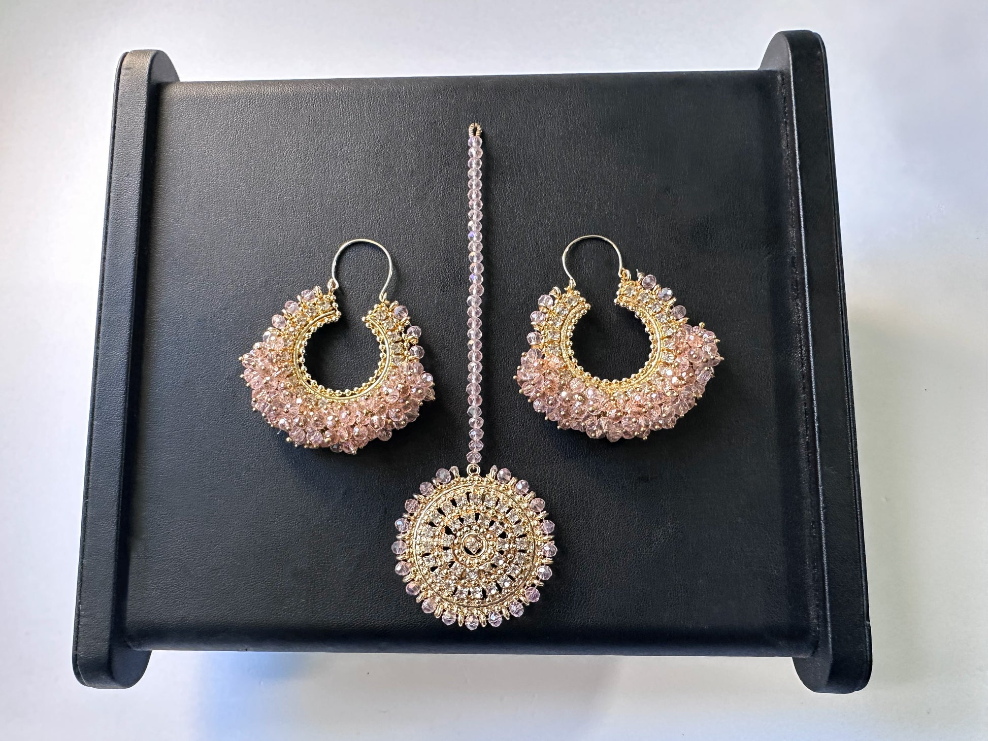 set of chand bali earrings and matching maang tikka in baby pink against a black display. trending Pakistani jewellery