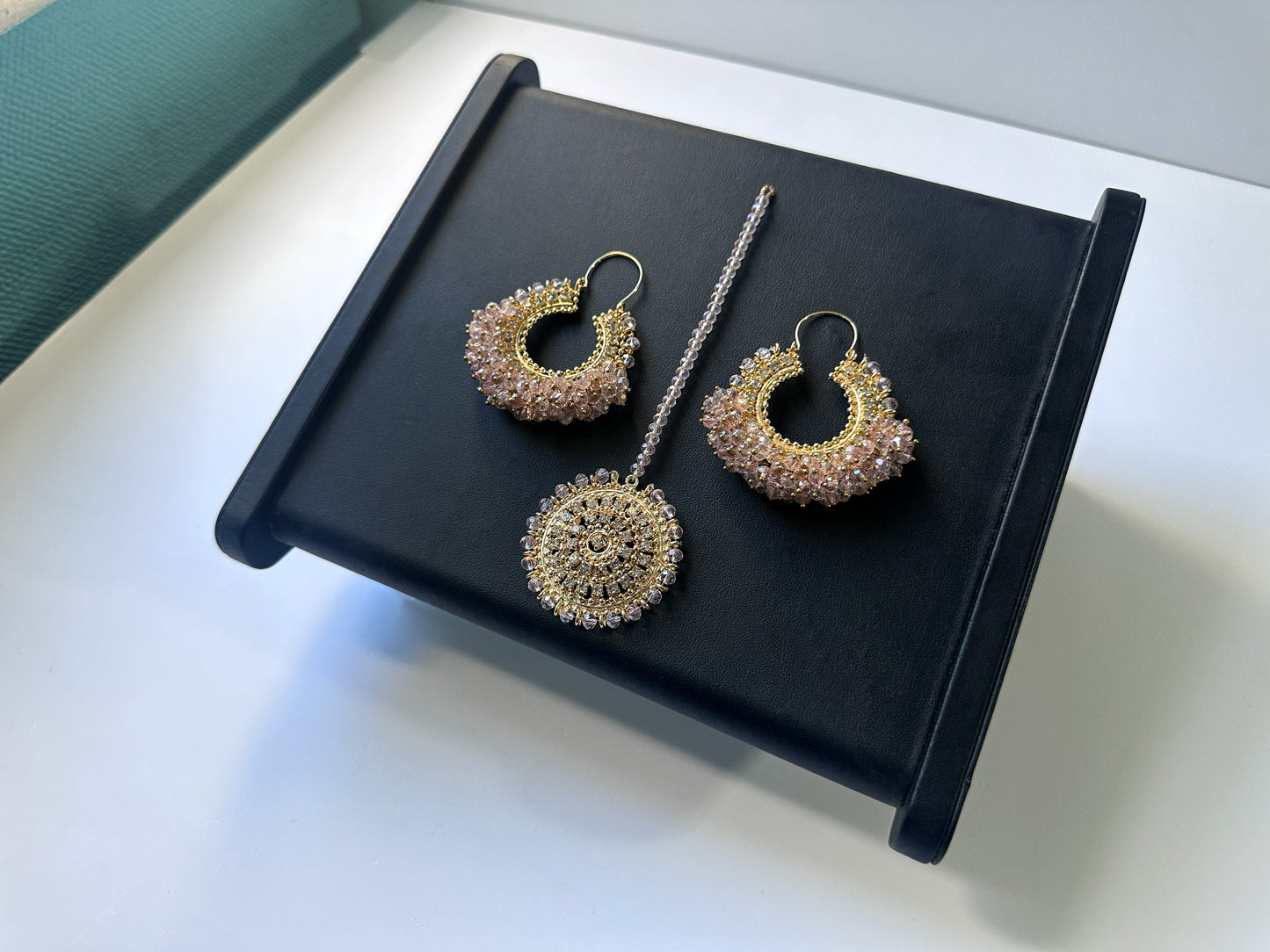 top view of baby pink chand bali earrings tikka against a black display. trending pakistani jewellery