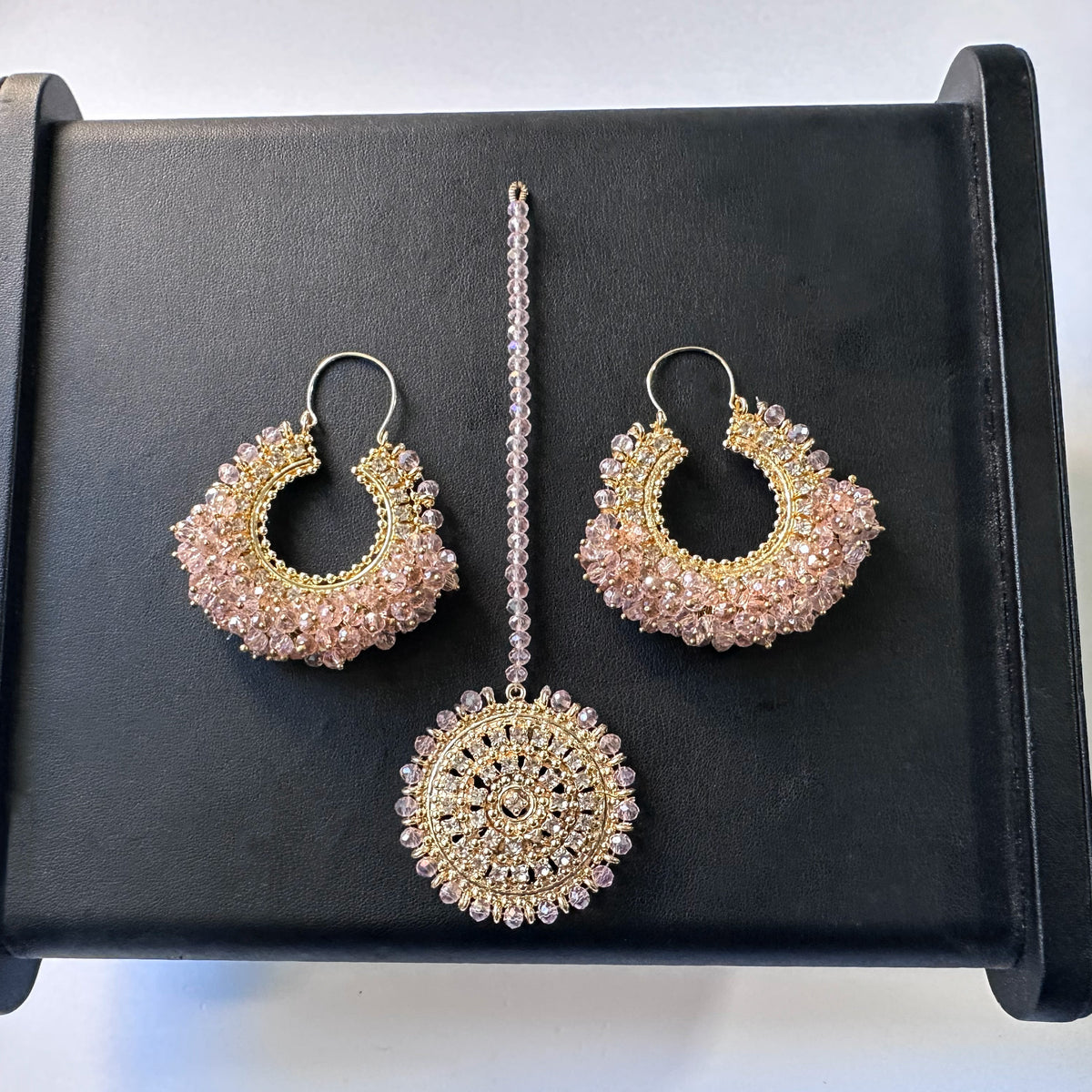 set of chand bali earrings and matching maang tikka in baby pink against a black display. trending pakistani jewellery