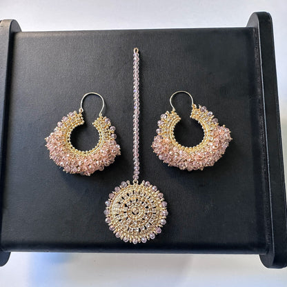 set of chand bali earrings and matching maang tikka in baby pink against a black display. trending Pakistani jewellery