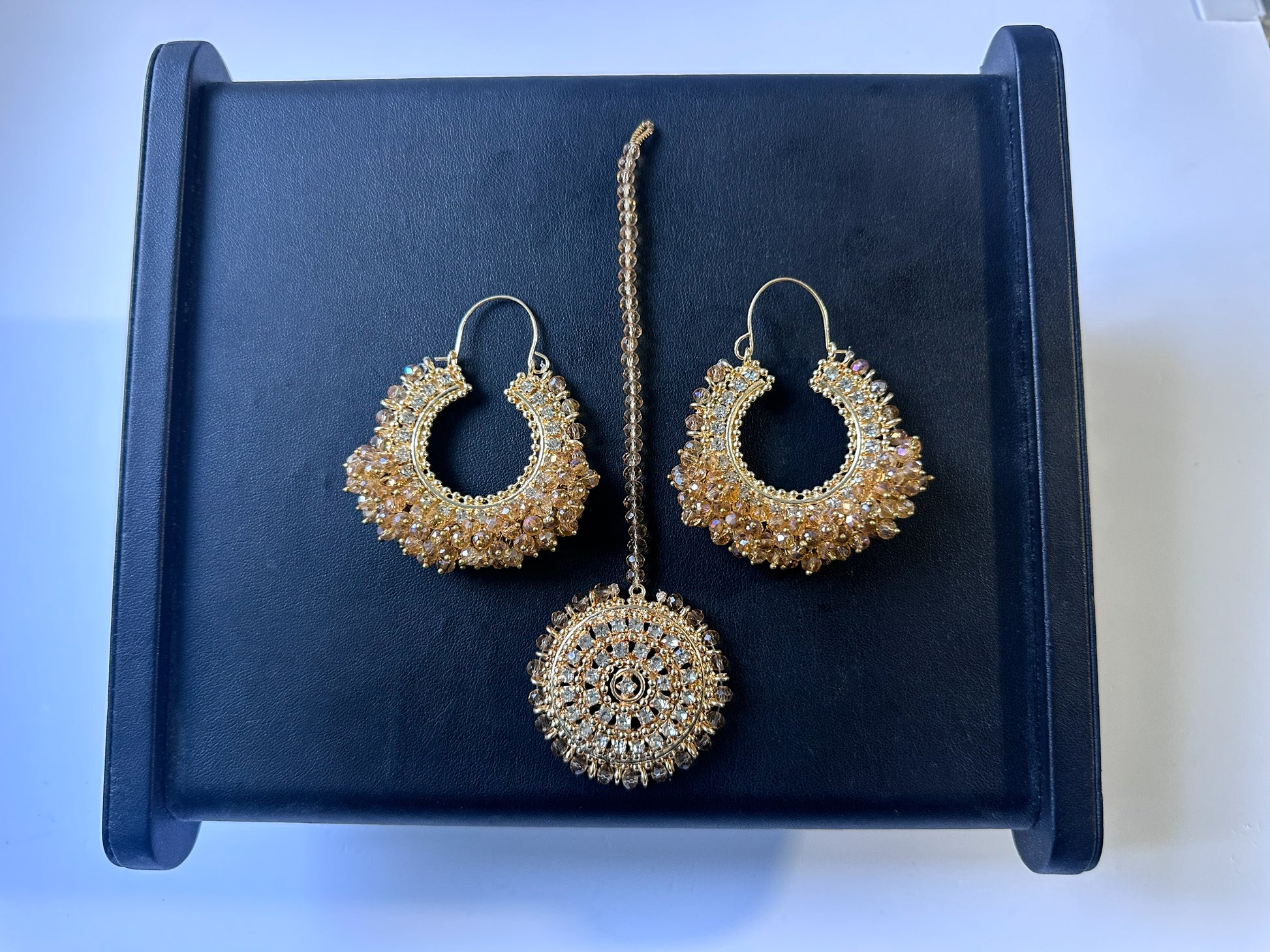 Gold hoop earrings and maang tikka on a black display. Trending pakistani jewellery