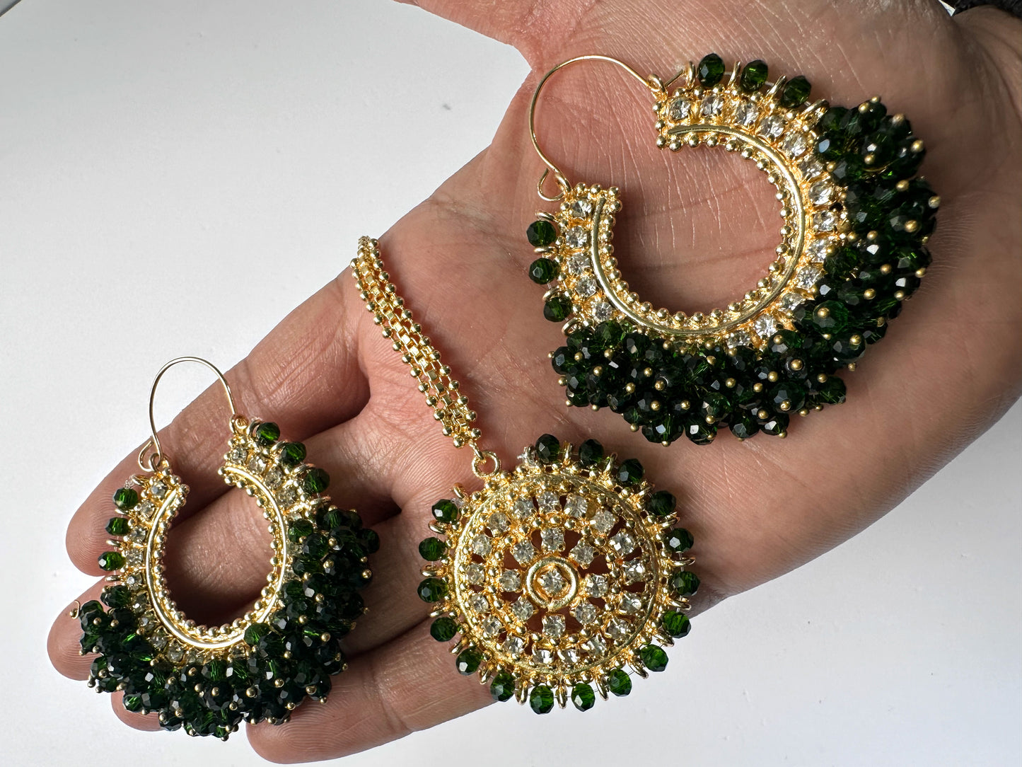 gold and green chand bali earrings tikka held in a hand - trending pakistani earrings tikka 