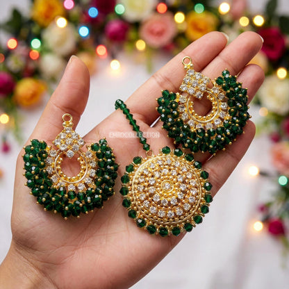 Gold and green chand bali earrings and tikka held in a hand with a festive background
