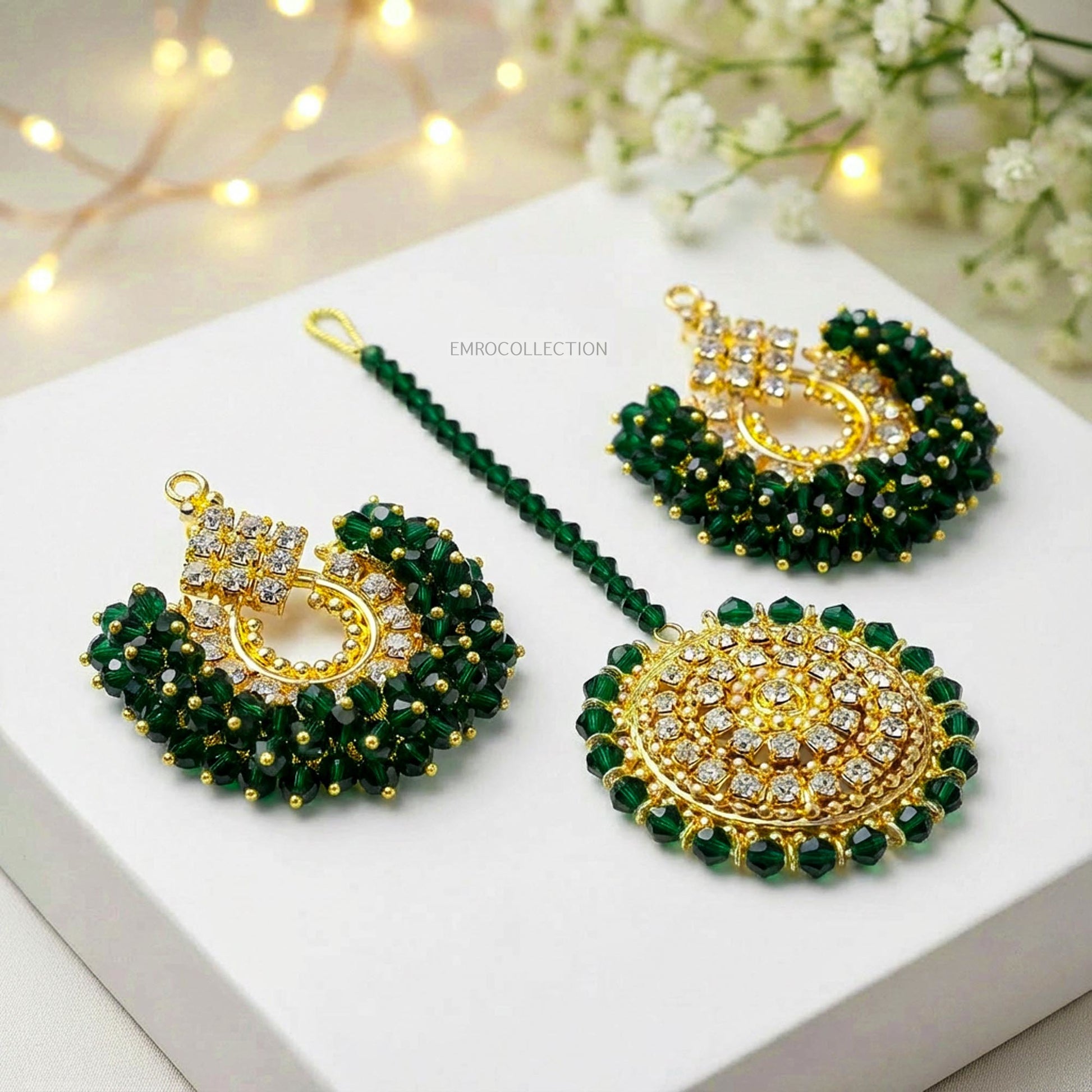 dark green earings tikka set on a white surface with decorative lights and flowers in the background.