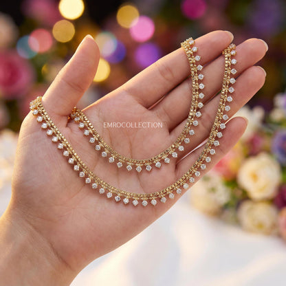 Gold anklets on a hand with a blurred floral background - Trending pakistani jewellery