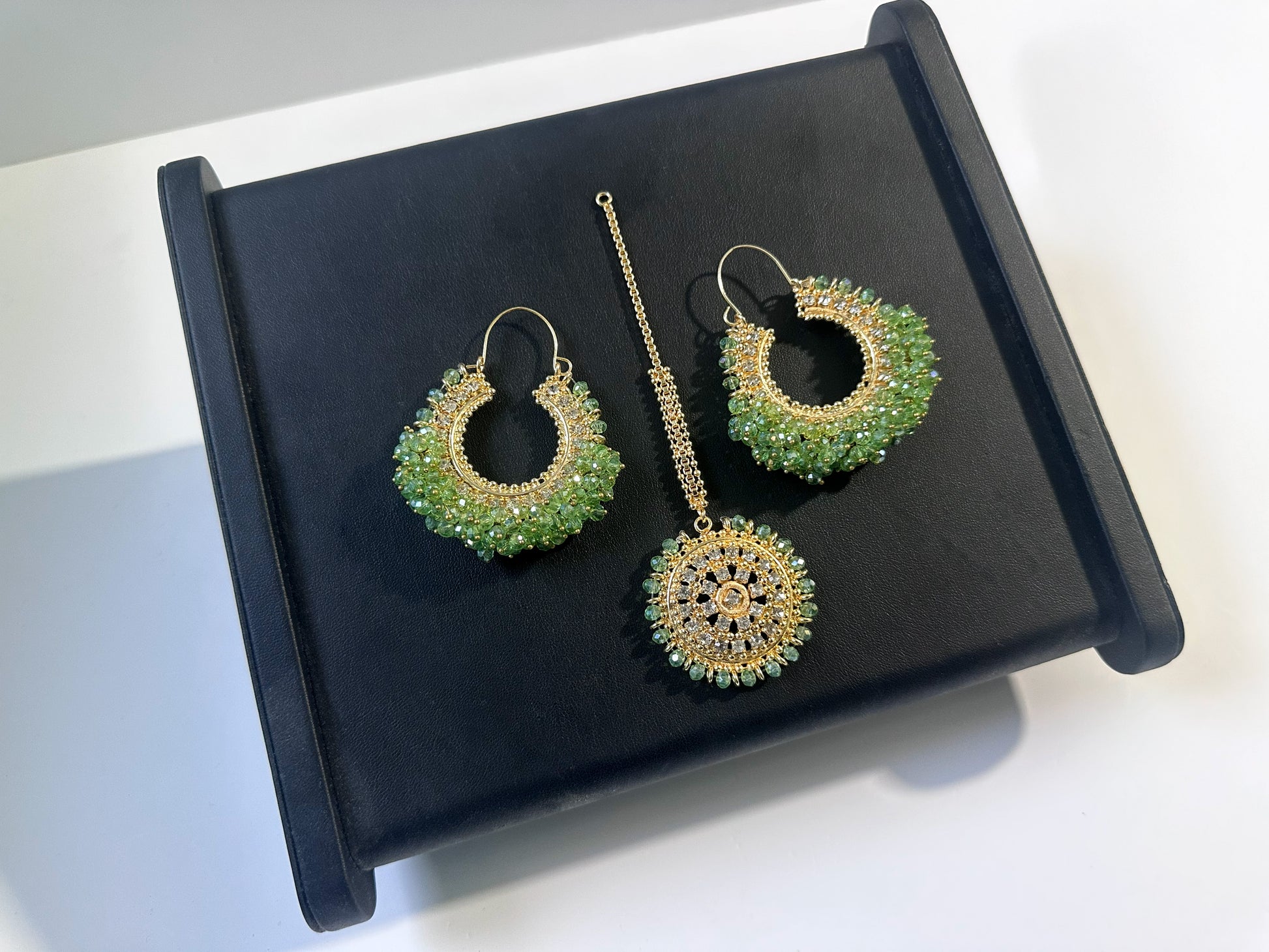 light green chand bali earrings and maang tikka on a black display. 