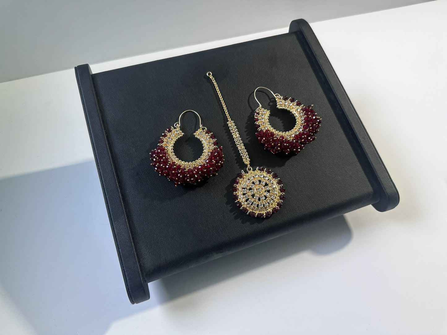 dark maroon chand bali earrings and maang tikka set against a dark display - trending pakistani erarrings tikka set