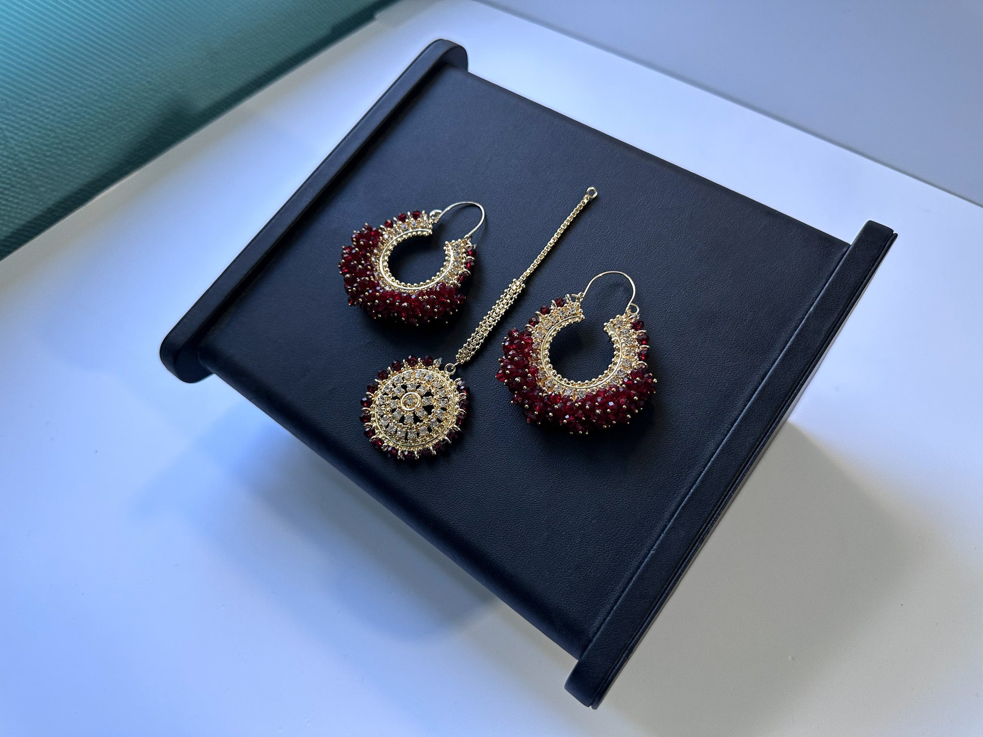 Maroon bali earrings and maang tikka against a black display. 