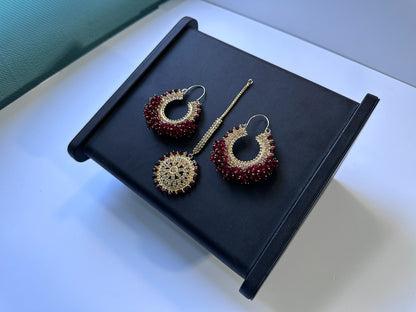 Maroon bali earrings and maang tikka against a black display. 