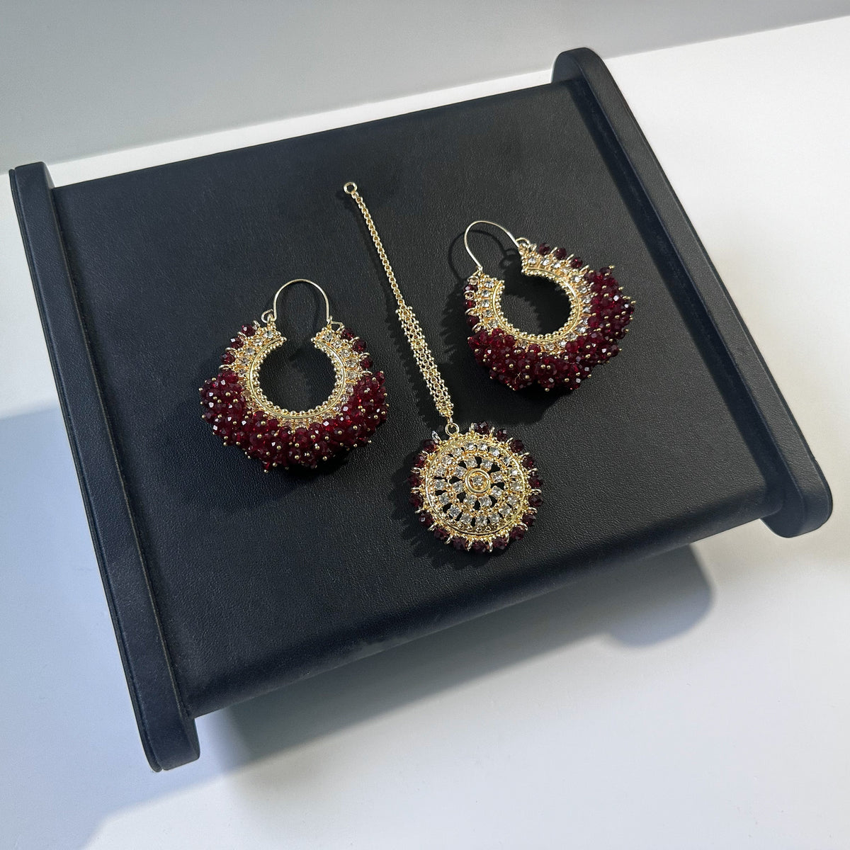 Dark maroon chand bali earrings and maang tikka set against a dark display - Trending pakistani erarrings tikka set