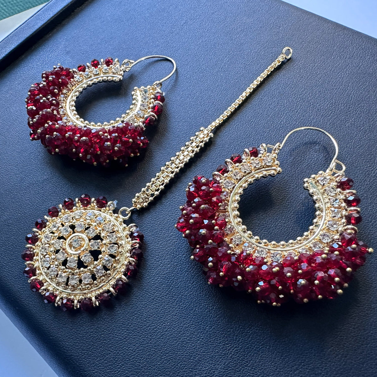 Side angle of maroon chand bali earrings tikka on a flat surface. Trending high quality pakistani jewellery