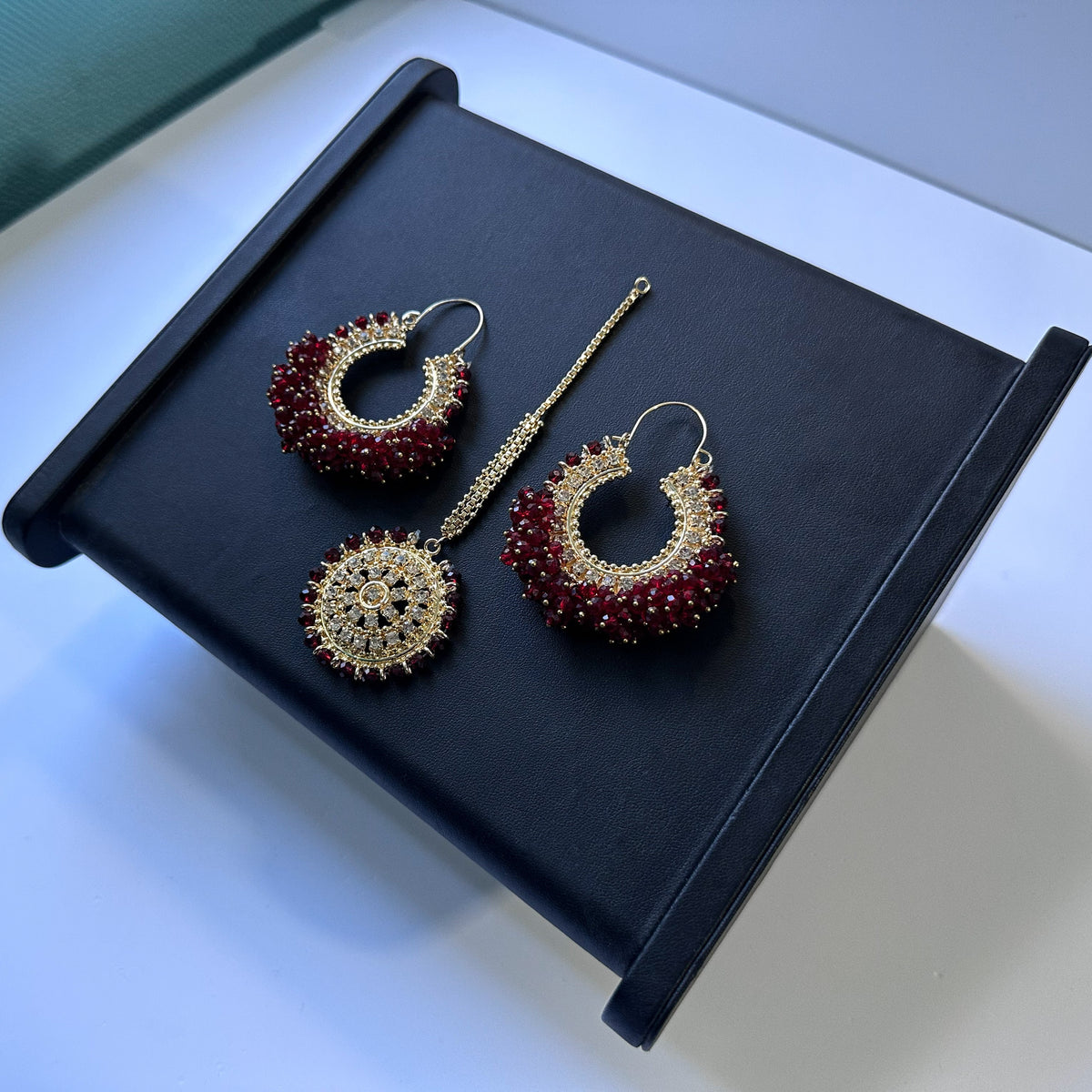 maroon bali earrings and maang tikka against a black display. 