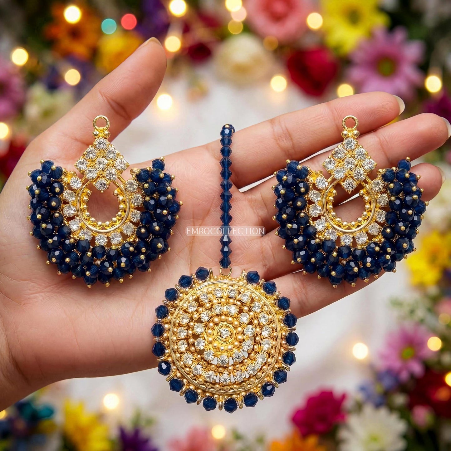 hand holding gold and navy blue earrings tikka set with colorful blurred background