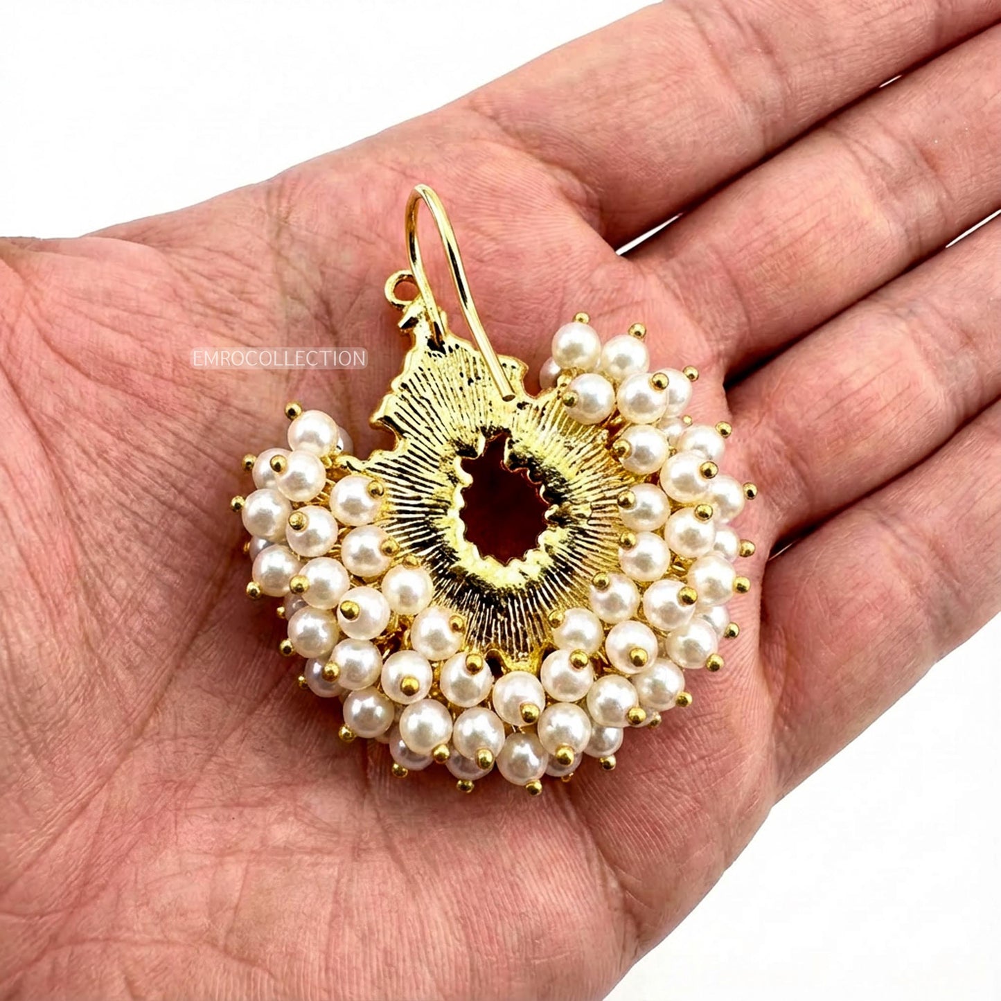 gold and pearl earring held in a hand against a white background