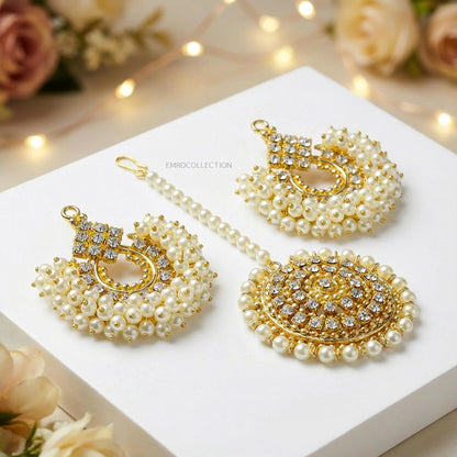 Gold and pearl jewelry set on a white surface with floral decorations and string lights in the background.