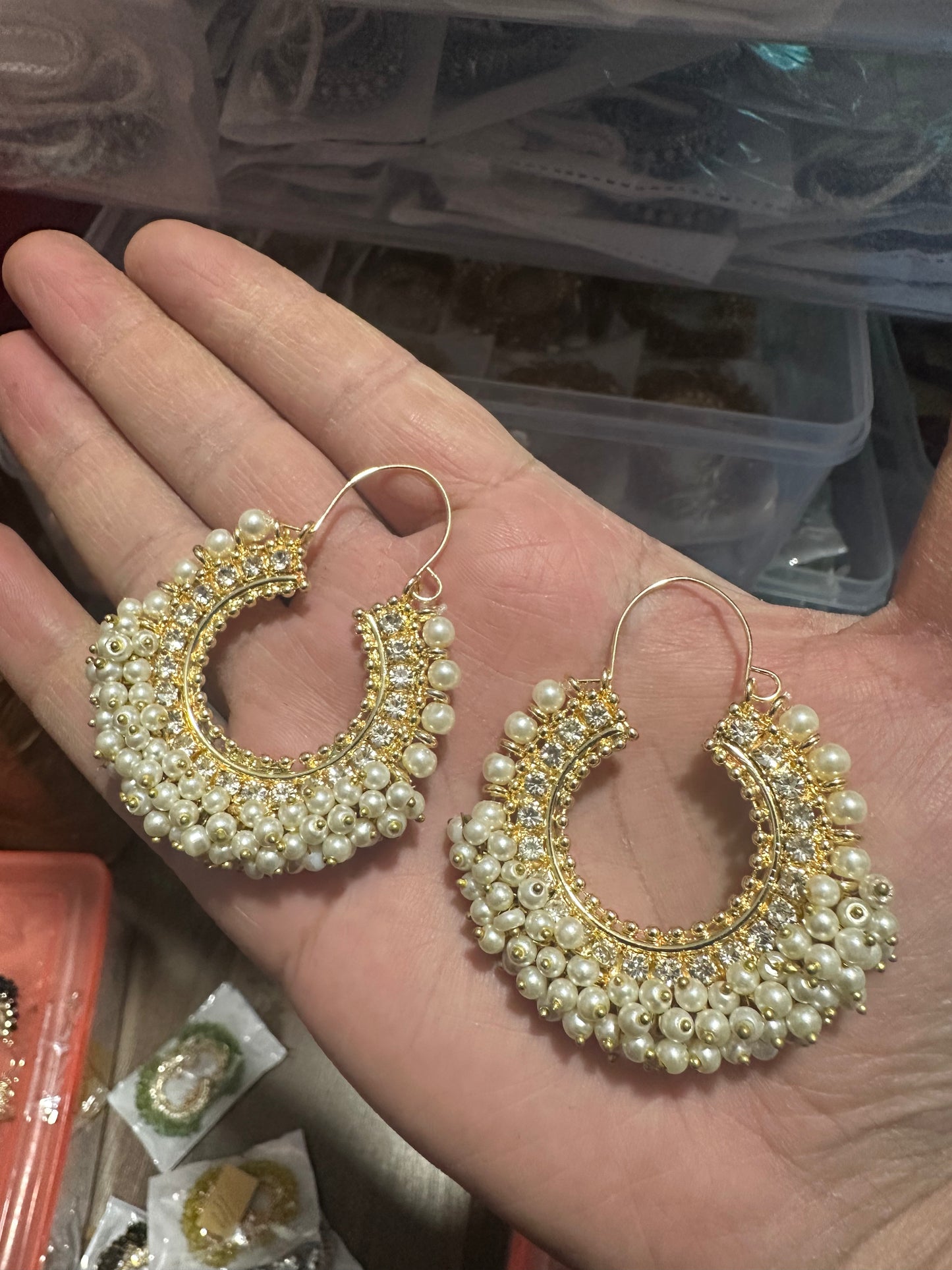 gold and pearl earrings held in a hand with a blurred background