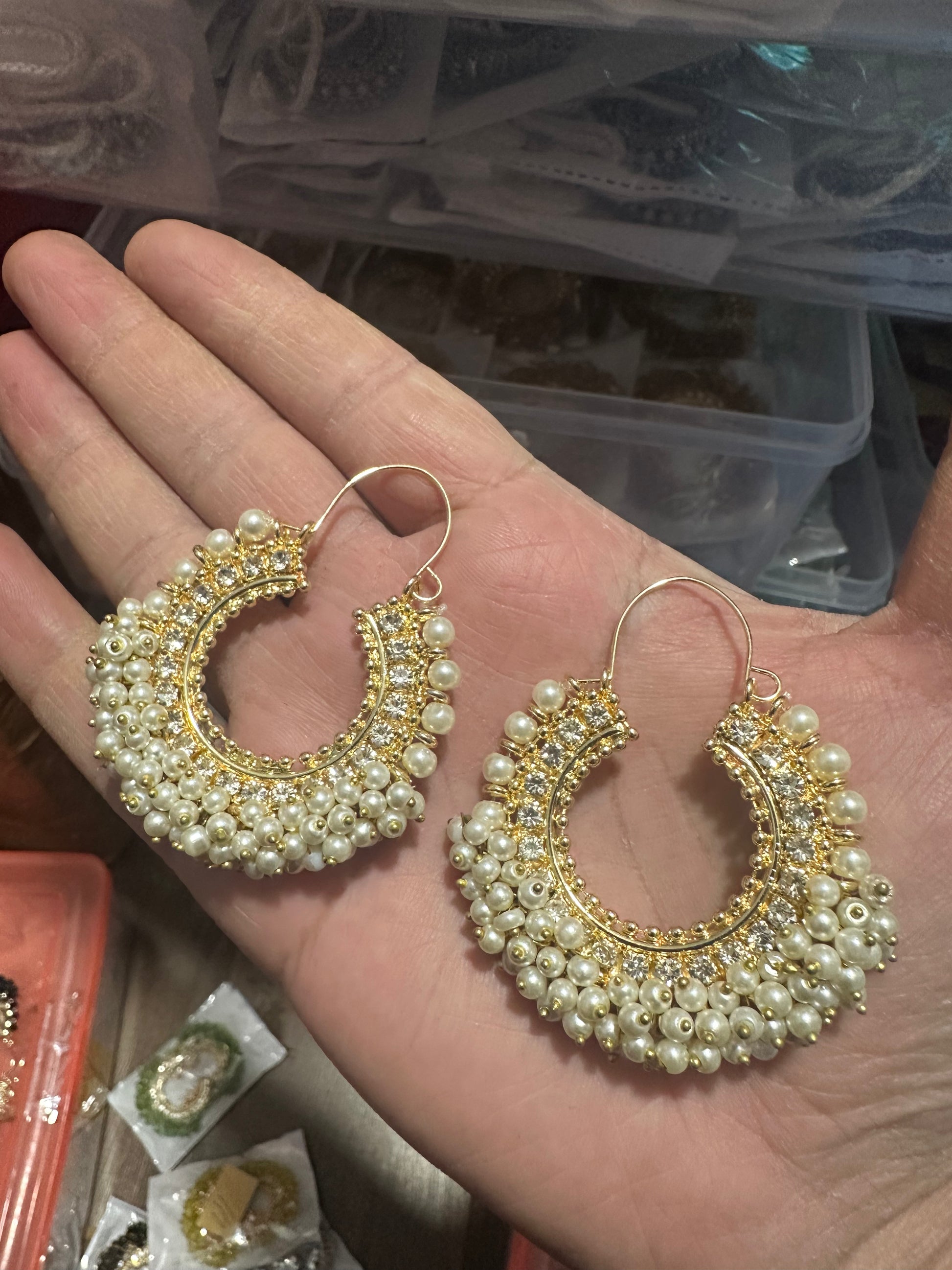 Gold and pearl earrings held in a hand with a blurred background