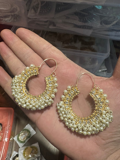 Gold and pearl earrings held in a hand with a blurred background