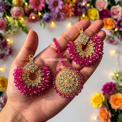Hand holding pink and gold earrings tikka with a floral background - trending pakistani earrings tikka