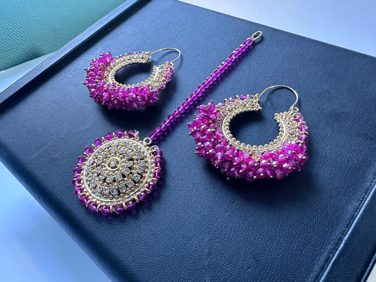 traditional shocking pink chand bali earrings and maang tikka on a dark display. trending pakistani jewellery