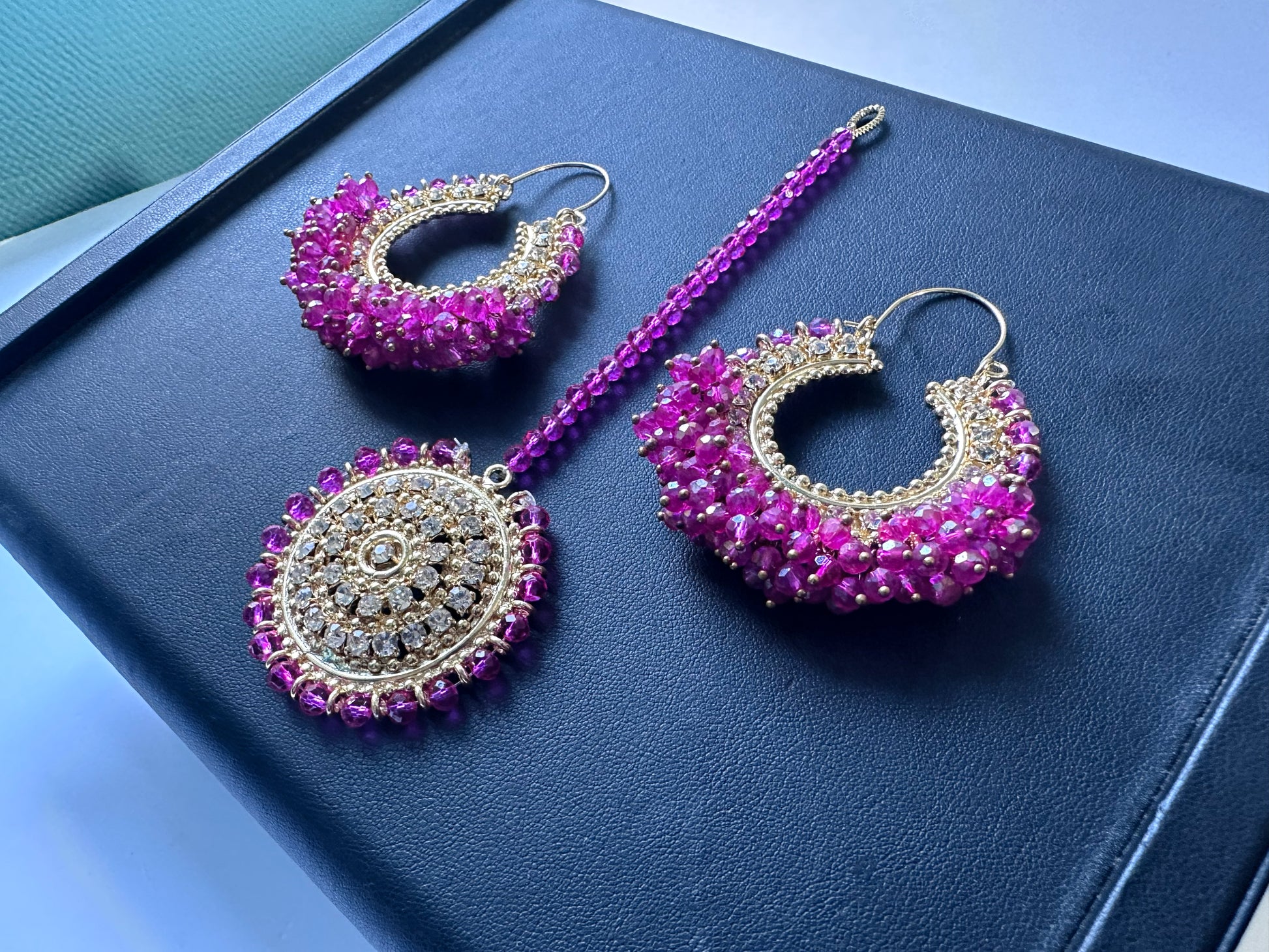 Traditional shocking pink Chand Bali earrings and Maang Tikka on a dark display. trending pakistani jewellery